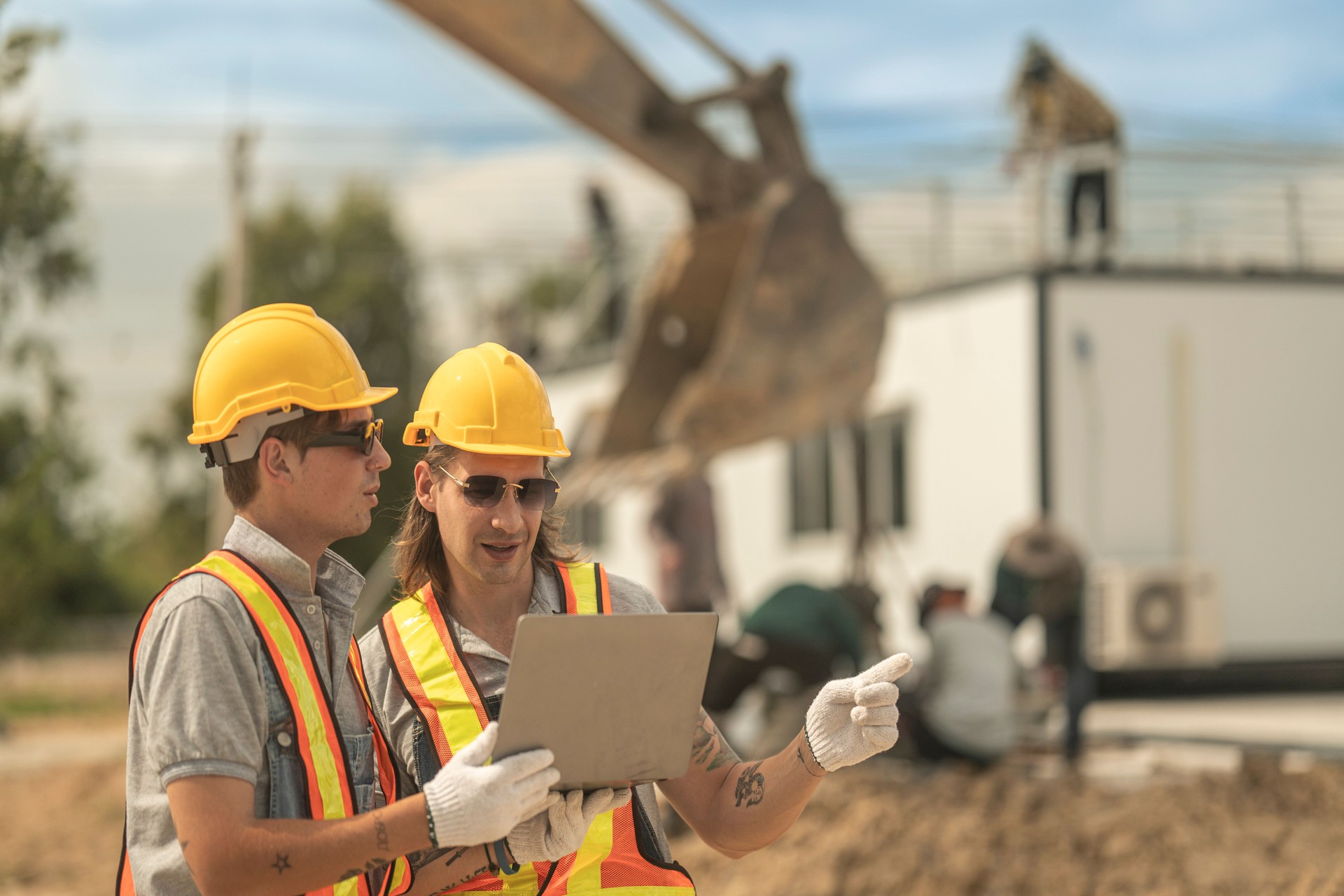 Workers in safety vests and helmets reviewing construction plans at a job site, highlighting teamwork, efficiency, and project execution for infrastructure and industrial development.