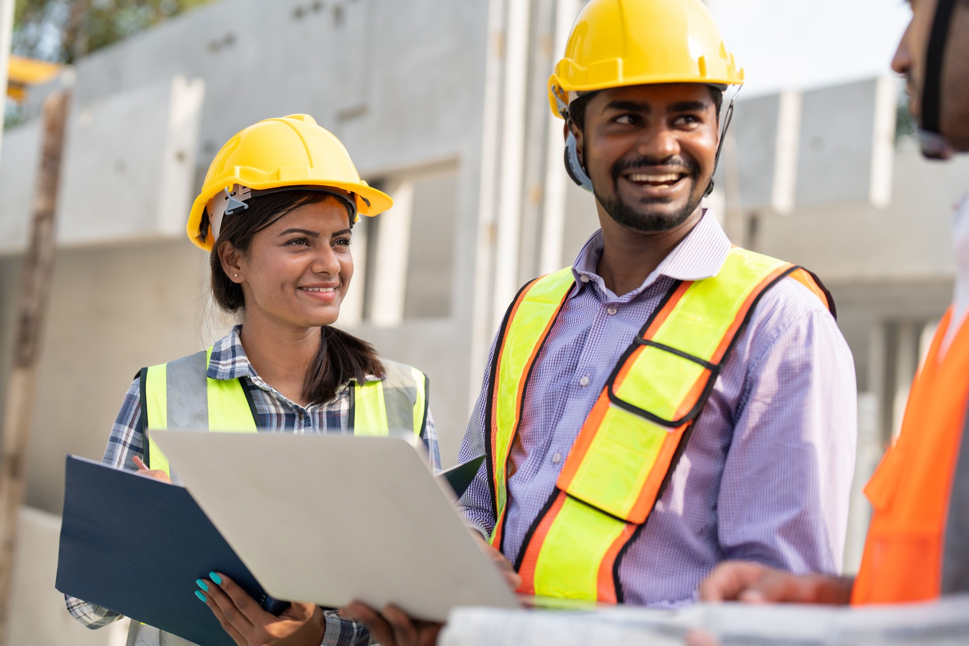 Team of construction engineers wearing vest and helmet safety discussing project at construction site.Group Indian foreman with laptop, paperwork working at factory marking precast concrete wall.