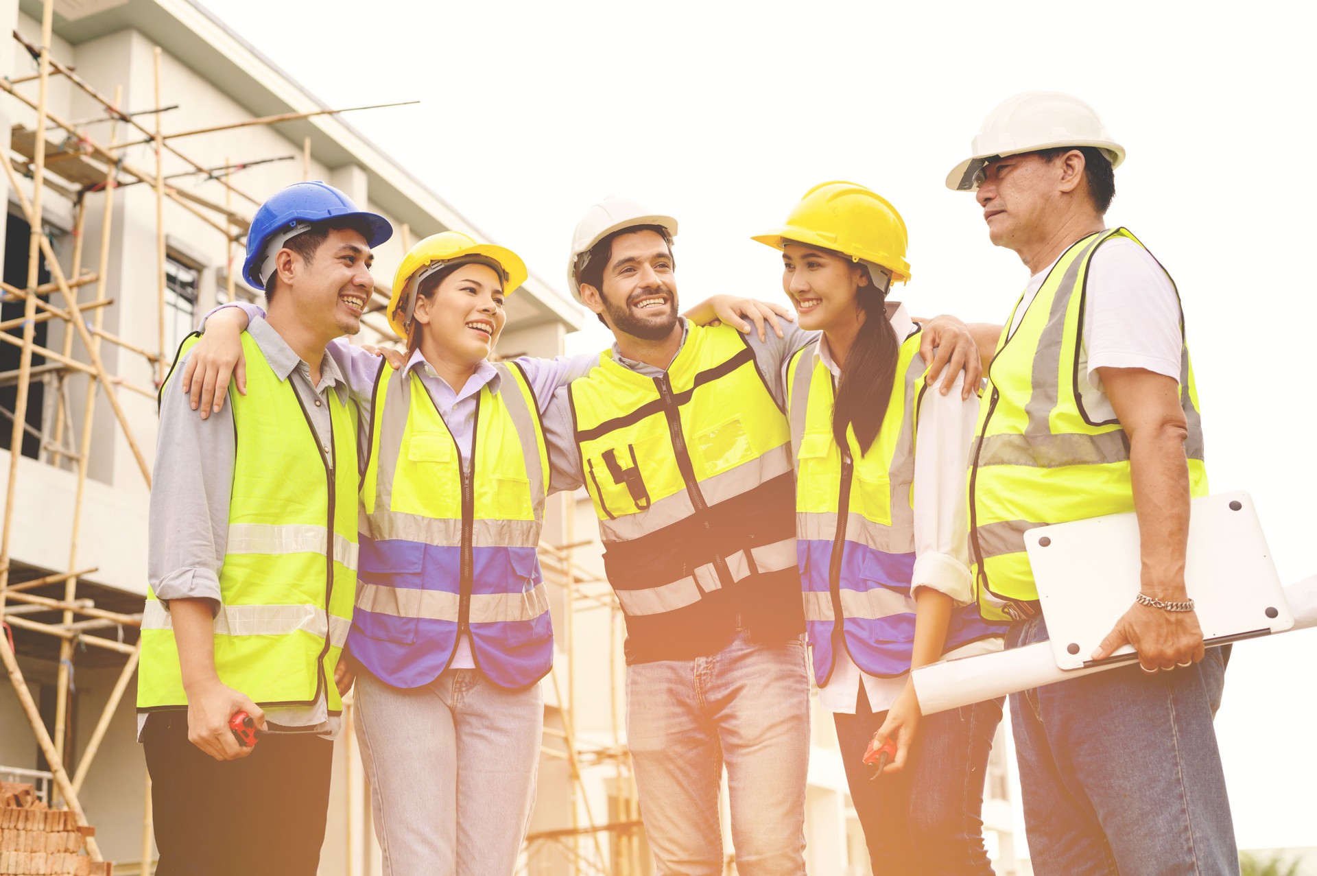 Group of happy contractors, engineers and formats in safety vests with helmets stand on the under-construction building site. teamwork concept.