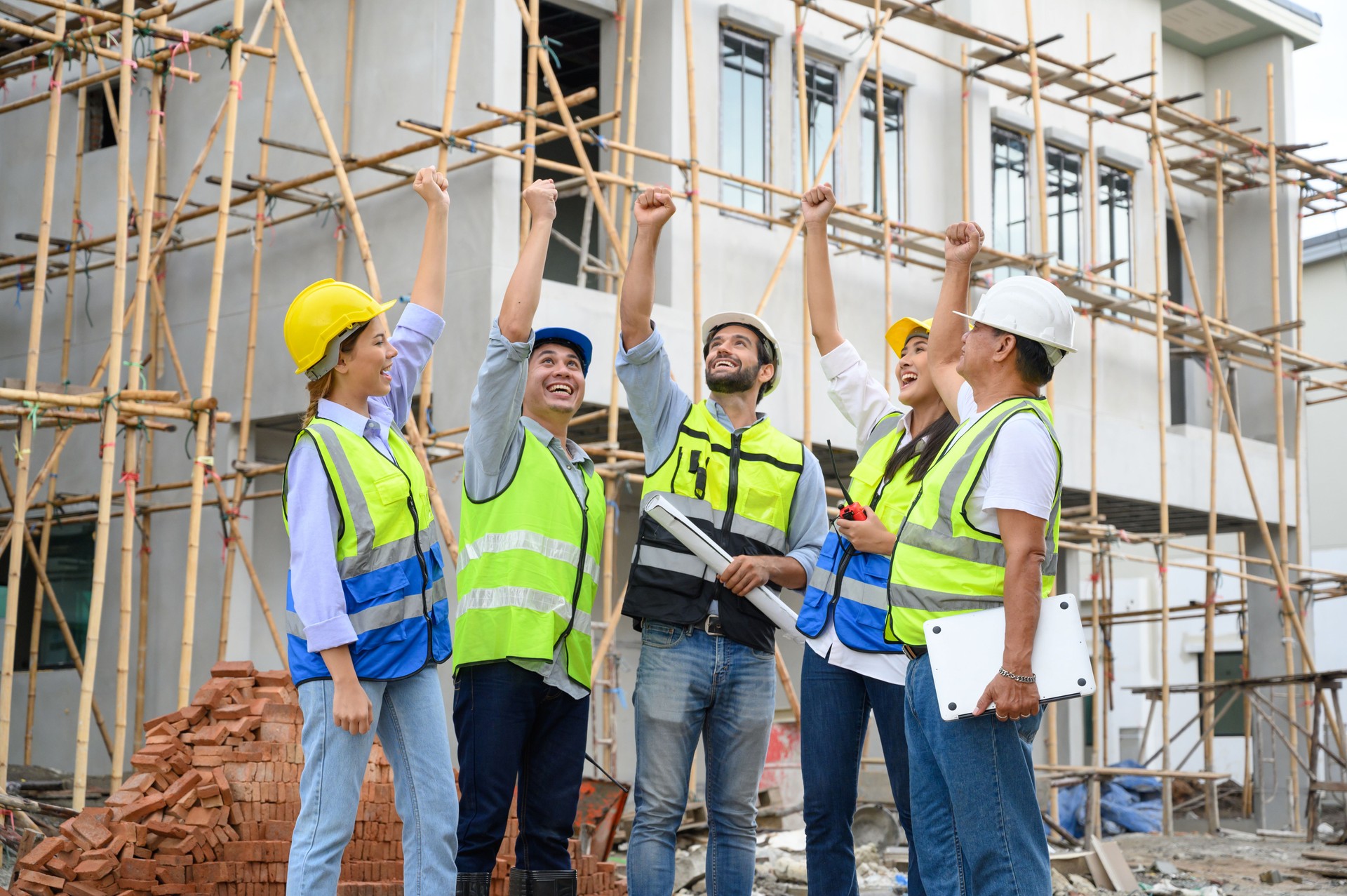 Group of contractors, engineers and formats in safety vests with helmets hands up to work together to successfully complete a construction project on construction site. cooperation and success concept.